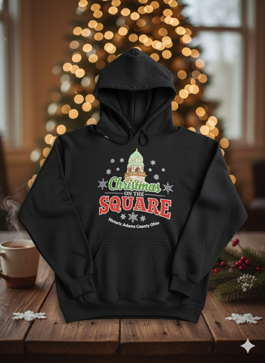 Black hoodie with 'Christmas on the Square' design in front of a decorated Christmas tree.